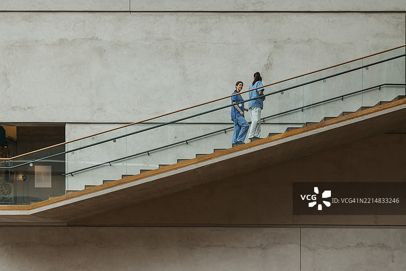 几位不同种族的女性医生在医院大楼内一边交谈一边走上楼梯。图片素材
