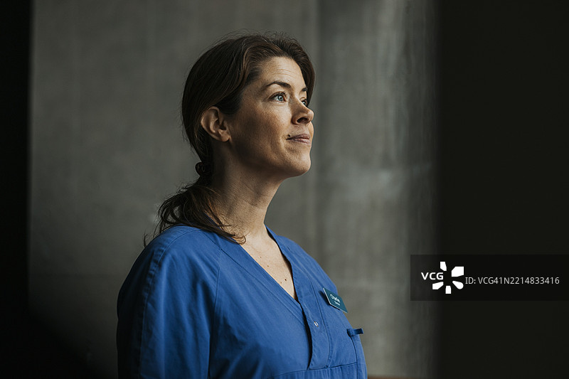 微笑的女性医护人员穿着医疗制服，目光投向一旁。图片素材