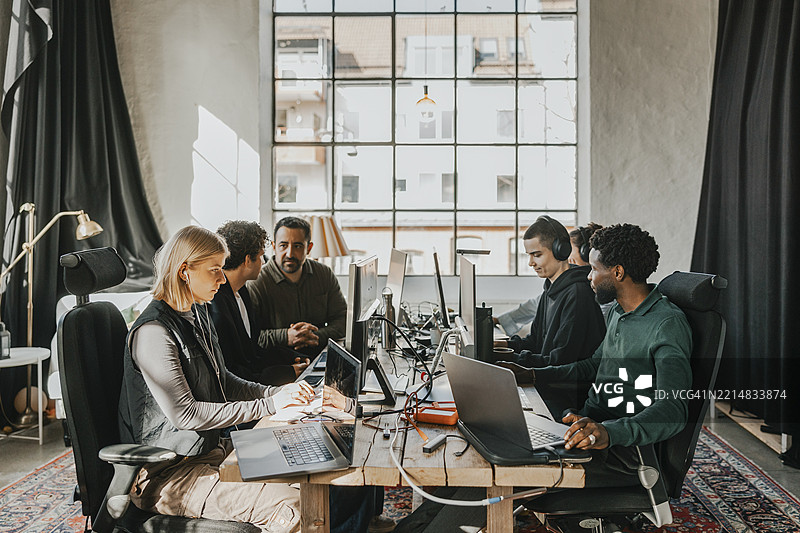 一群多种族的计算机专业人士在科技初创公司的办公室里坐在桌子旁使用台式电脑。图片素材