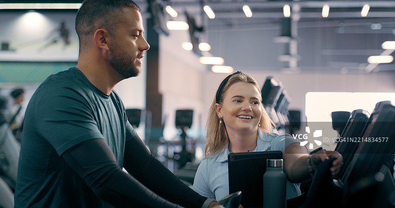 健身房里的私人教练，男士与健身自行车进行锻炼指导，监测进展或心肺支持。快乐的教练或平板电脑用于训练评估、跟踪表现或查看健身数据。图片素材
