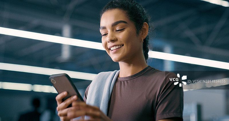 健身房内，女性与智能手机交流信息，在线沟通和健身应用。健康俱乐部，女性与手机聊天，享受锻炼或社交媒体的快乐与联系。图片素材