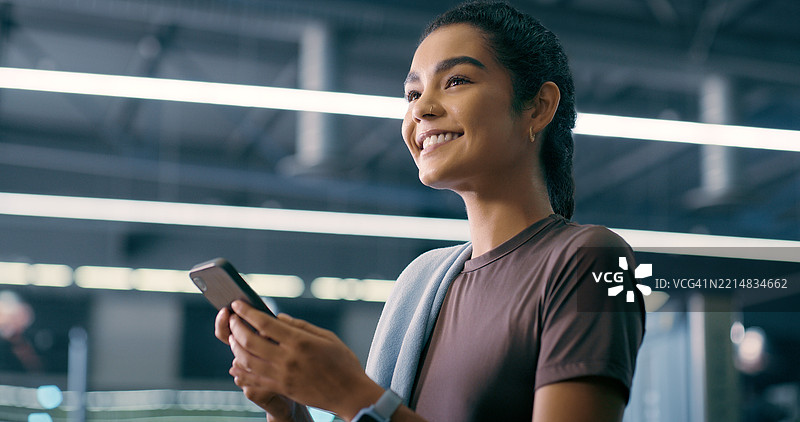 健身房，女性与智能手机，思考健身、在线交流和微笑锻炼。健康俱乐部，女性与手机应用的想法，用于聊天、锻炼表情包和社交媒体。图片素材