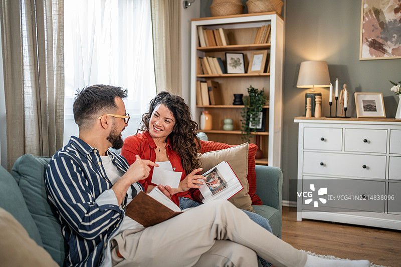 一对情侣微笑着在沙发上翻看相册，共享美好回忆图片素材