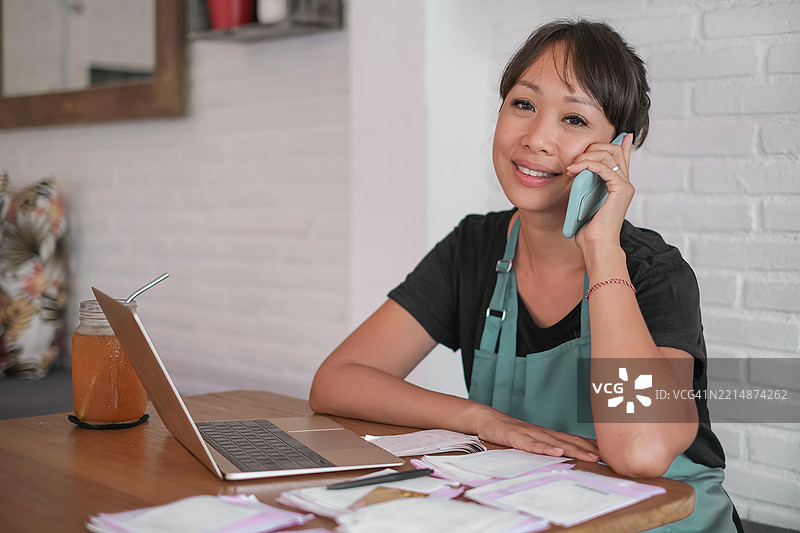 微笑的女性企业主一边打电话一边在笔记本电脑上工作图片素材