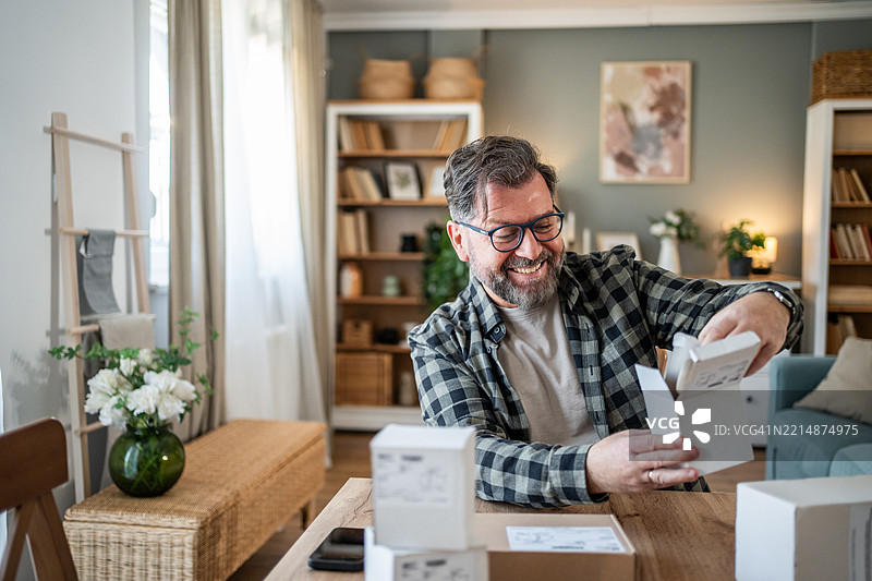 快乐的成熟男人在家中拆包裹图片素材