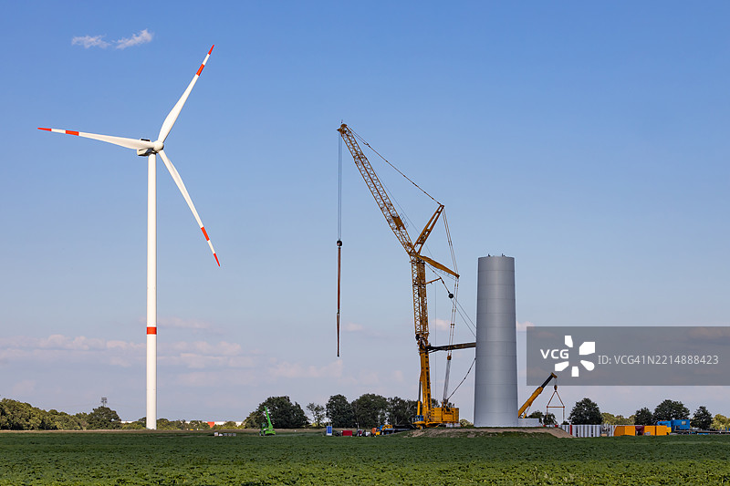 风力发电机建设工地，配有大型起重机和一台完工的风力发电机图片素材