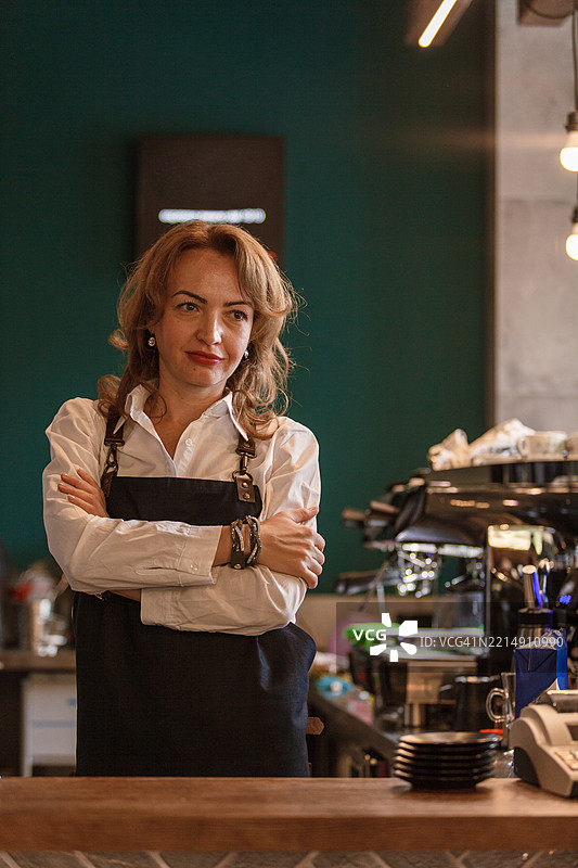 自信的女性咖啡师在咖啡店里双臂交叉站立图片素材