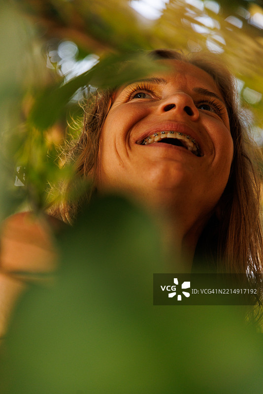 微笑的女人在自然阳光下透过树叶仰望的特写镜头图片素材