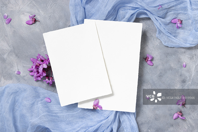 灰色背景上，野生紫色花朵旁的垂直空白卡片，春季婚礼样板的俯视图图片素材
