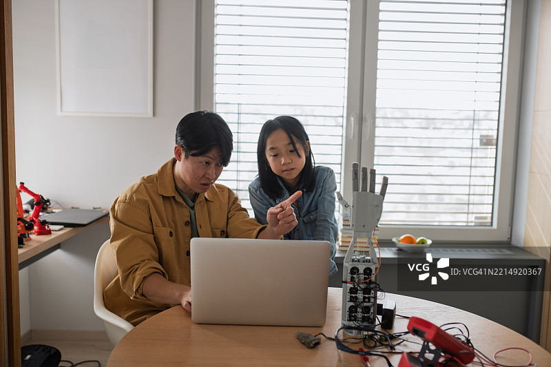 父亲在教女儿关于STEM、机器人技术，并讨论科技。图片素材