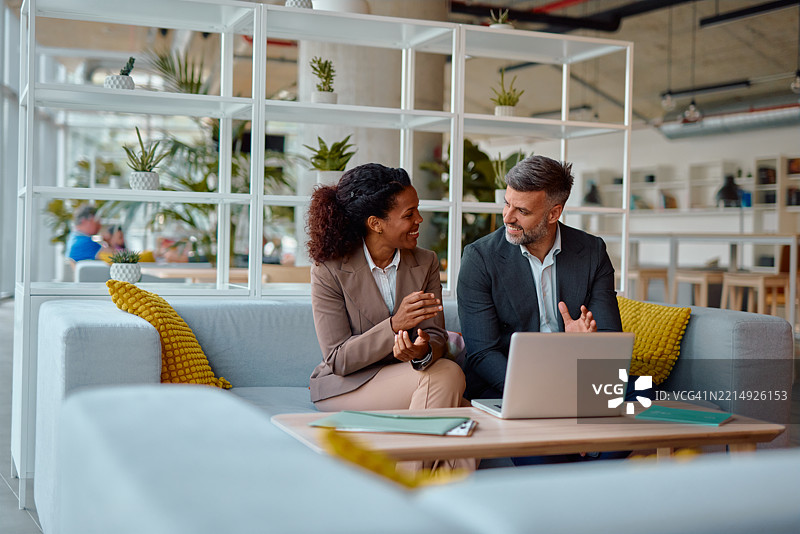 商业伙伴在现代办公室大堂讨论使用笔记本电脑图片素材