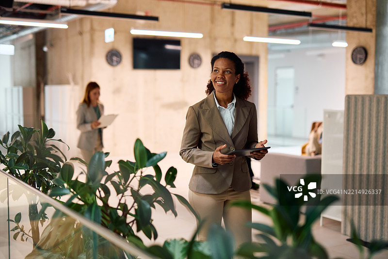 微笑的女商人手持数字平板在现代办公室内走动图片素材