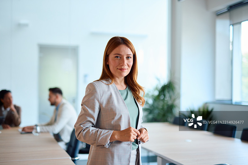 女商人在会议室内站着调整她的西装外套图片素材