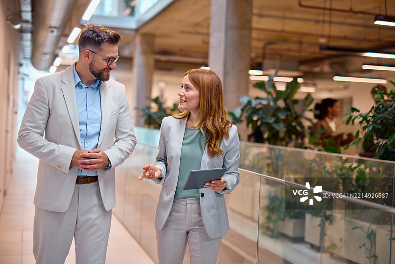 商务人士在现代办公室走廊中走动并交谈图片素材