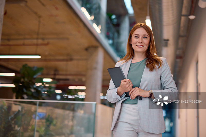 微笑的女商人在现代办公大楼中手持平板电脑图片素材