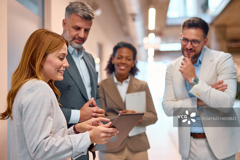 女商人在办公室走廊向同事展示平板电脑图片素材
