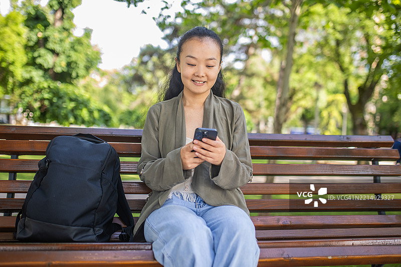 一位游客坐在公园长椅上，使用手机查看城市的在线地图和新目的地。图片素材