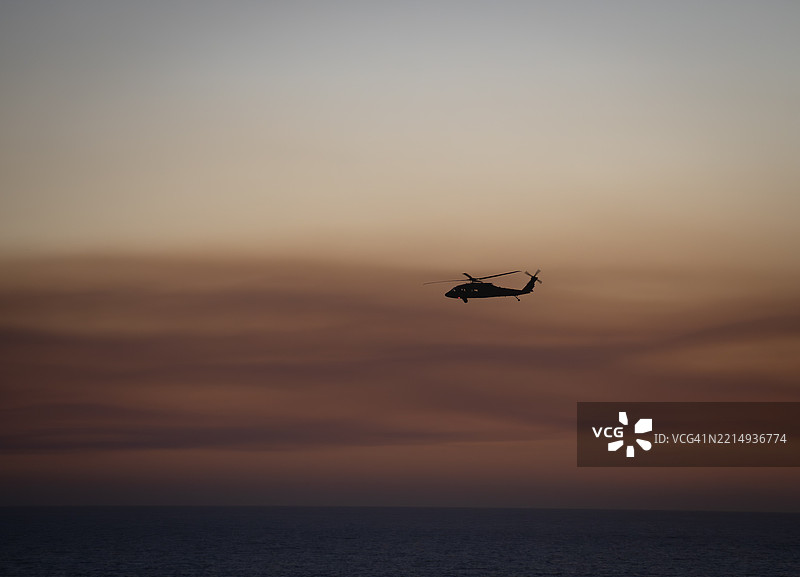加利福尼亚州，美国，夕阳下海面上飞行的直升机剪影图片素材