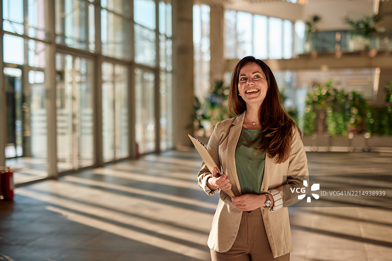 微笑的女商人在现代办公室大堂里手持夹板图片素材