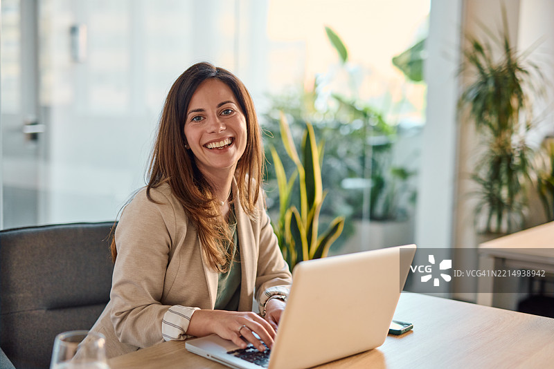 年轻女商人在现代办公室微笑着使用笔记本电脑。图片素材