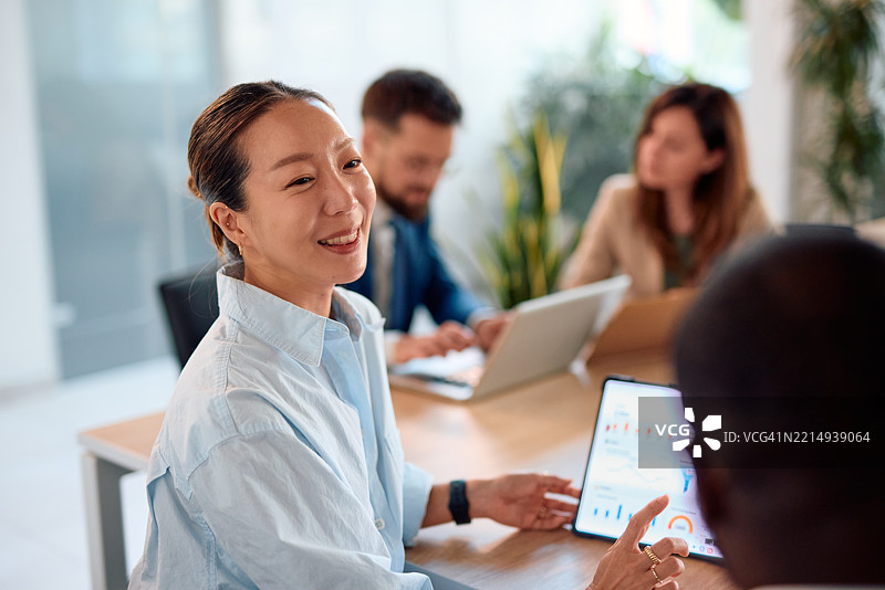 亚洲女商人在办公室会议中与同事讨论平板上的数据图片素材