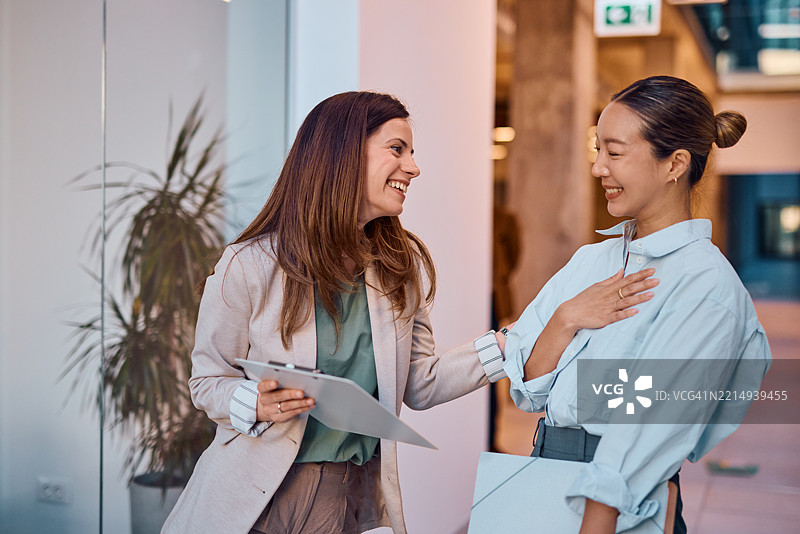 两位女商人在办公室走廊里欢笑交谈图片素材