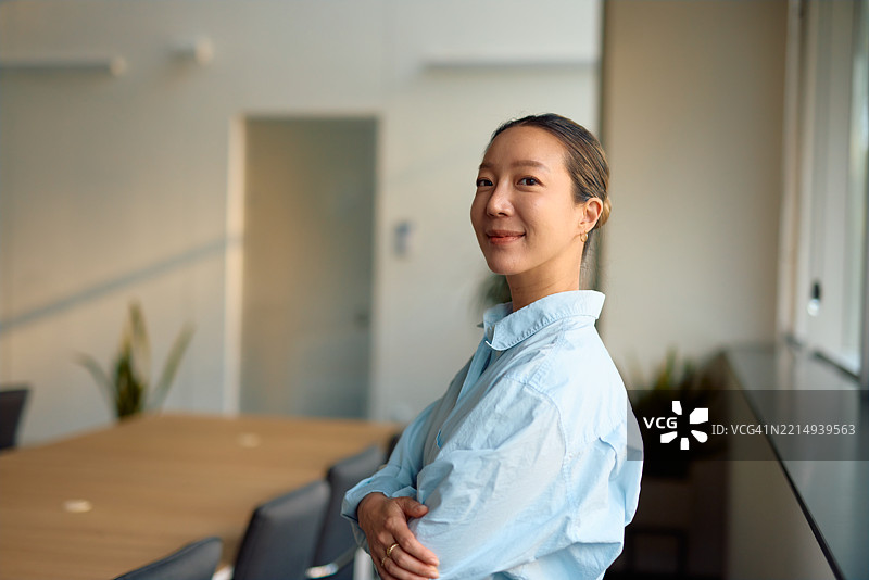 年轻的亚洲女商人在现代办公室微笑并交叉双臂图片素材