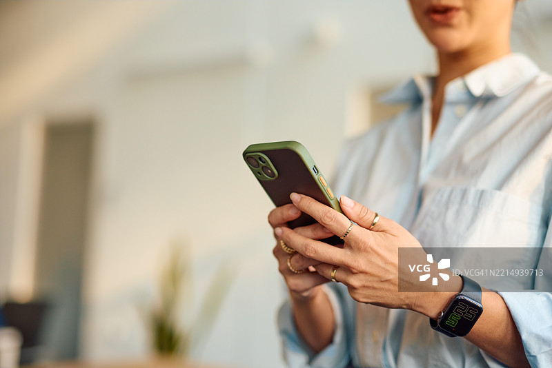 商务女性正在使用智能手机发送信息，并佩戴智能手表。图片素材