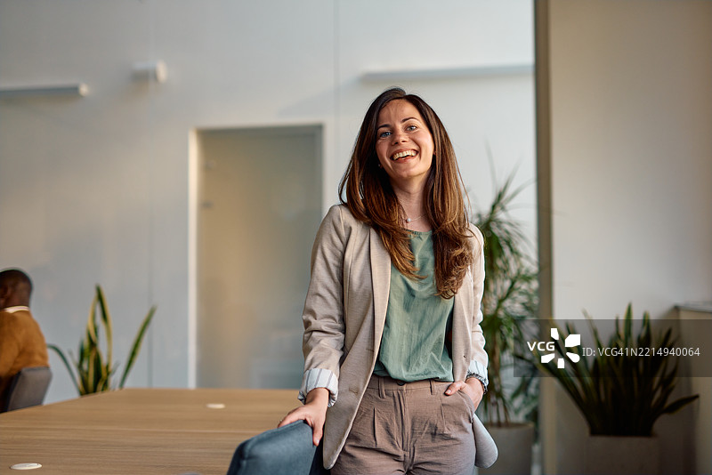 年轻女商人在现代办公室微笑，手插在口袋里图片素材