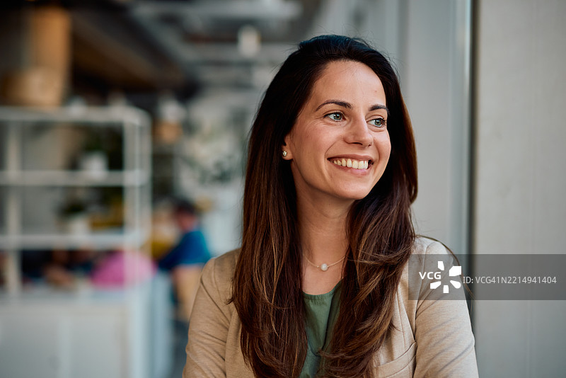 年轻女商人在咖啡馆工作时微笑并望向一旁图片素材