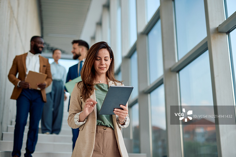 女商人在办公室走廊中与同事们走动时使用数字平板电脑图片素材