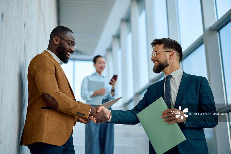两位商人在现代办公大楼内握手庆祝成功交易图片素材