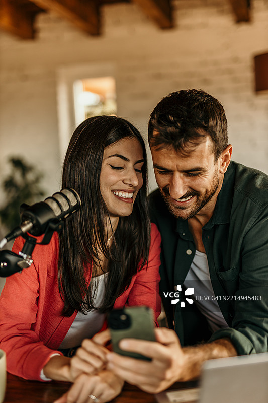 两位年轻的内容创作者正在录制播客并浏览智能手机图片素材