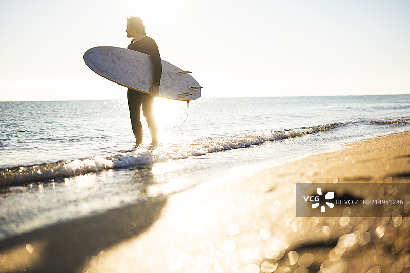 海滩假期。冲浪者在金色时光中进入海洋图片素材
