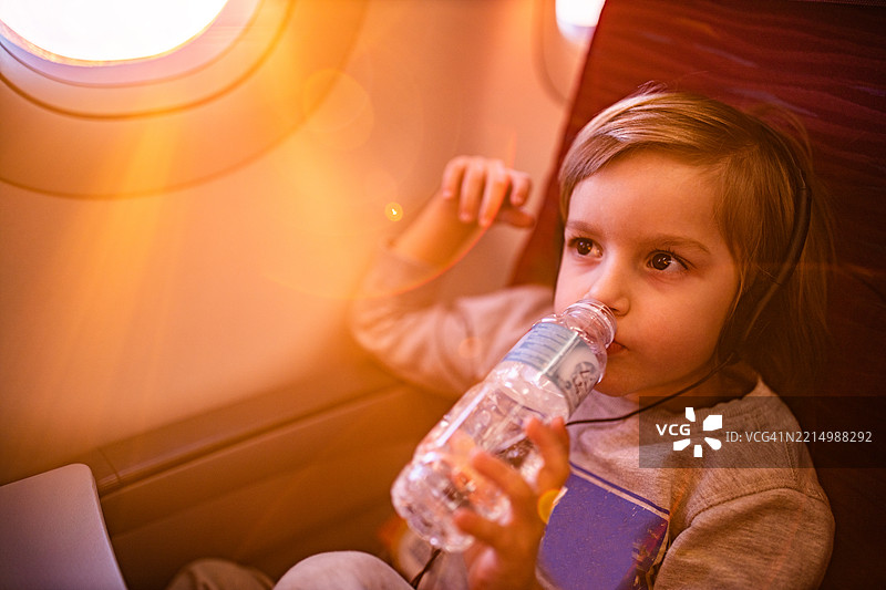 可爱男孩在飞机上喝水并听音乐。图片素材