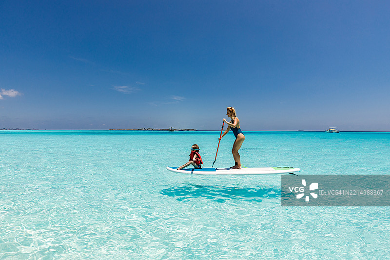 快乐的母亲和她的小男孩在夏日的海上站立划水。图片素材