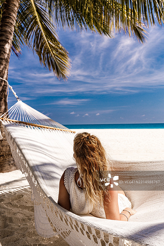 女人在海滩上吊床上放松的背影。图片素材