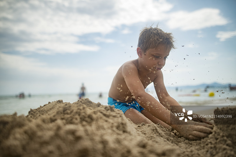 小男孩兴奋地挖沙并扔沙子，正在建造城堡。图片素材