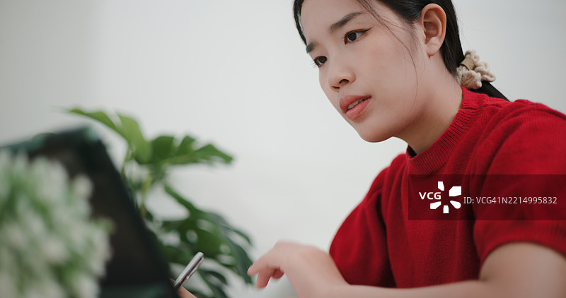 年轻的亚洲女性通过在线平台在数字平板上学习投资。图片素材