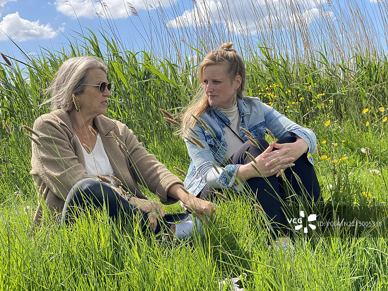母亲和女儿紧密相依坐在低洼地带。图片素材