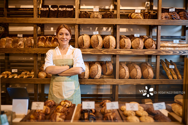 自信的女面包师在她的面包店里双臂交叉摆姿势图片素材