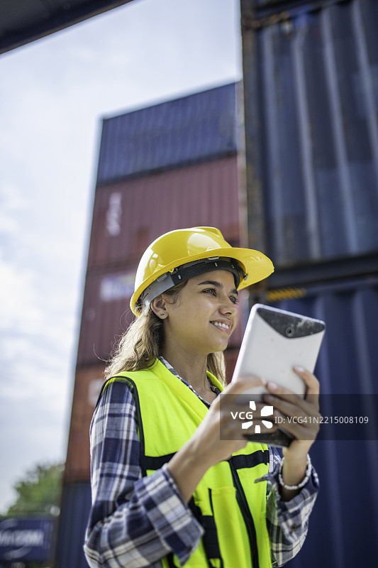 拉丁裔女性工程师在货物集装箱场使用数字平板电脑图片素材