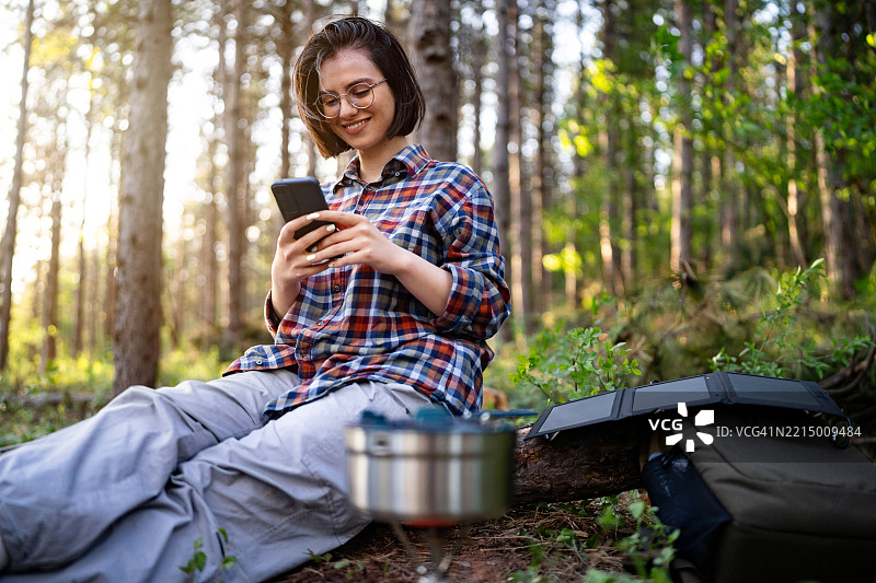 年轻女性在风景如画的森林露营时使用智能手机图片素材