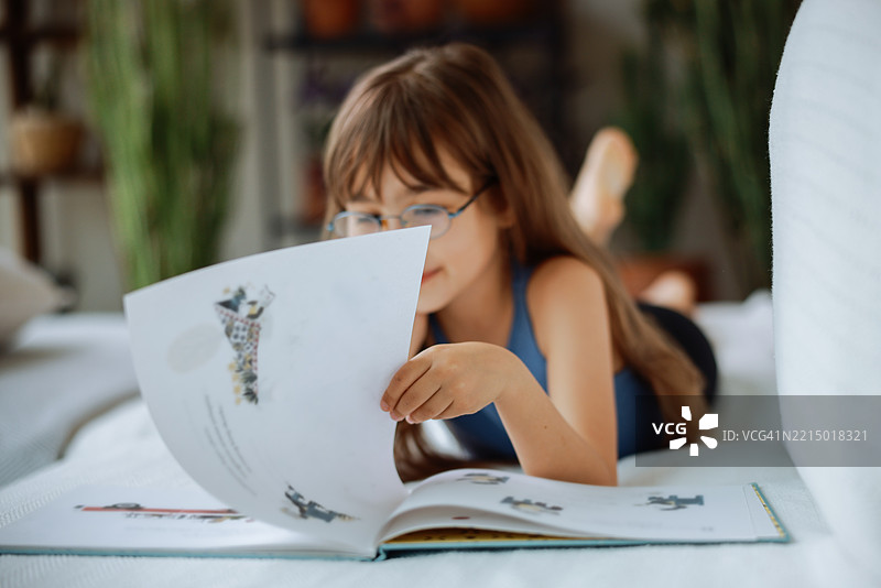 美丽的小女孩躺在沙发上看书。图片素材