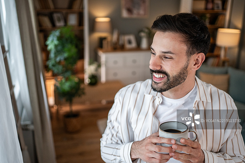 年轻男子在家窗边微笑着喝咖啡图片素材