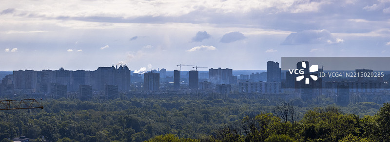 城市天际线从森林中显现，笼罩在多云的天空下图片素材