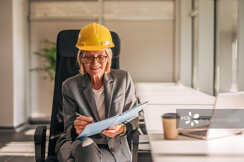 资深女性建筑师在现代办公室审查蓝图图片素材