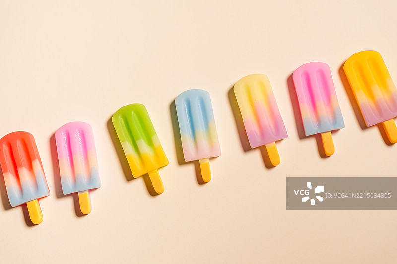 五彩缤纷的冰棒斜放在淡黄色背景上图片素材