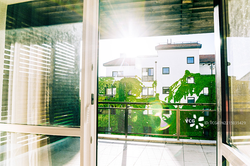 阳光明媚的日子，开放的阳台门俯瞰着被绿色常春藤覆盖的建筑。图片素材