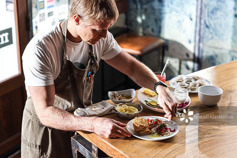 一位厨师在明亮的餐厅里的木桌上准备餐点图片素材